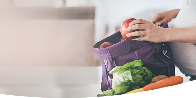 Petite pregnant woman unpacking a reusable grocery bag of fresh fruits and vegetables.